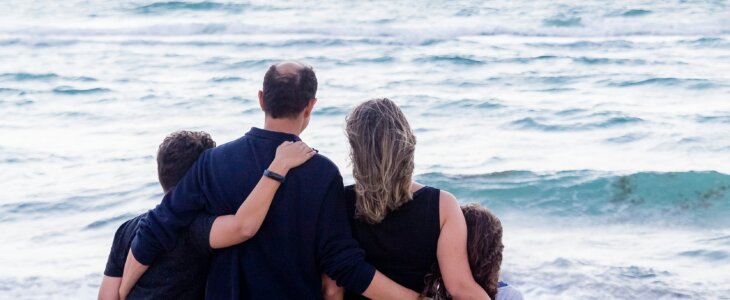 family standing on the beach looking at the water