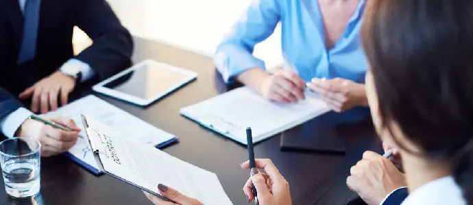 3 business people sitting at a desk with papers to sign