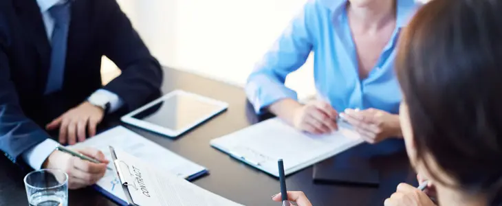3 business people sitting at a desk with papers to sign