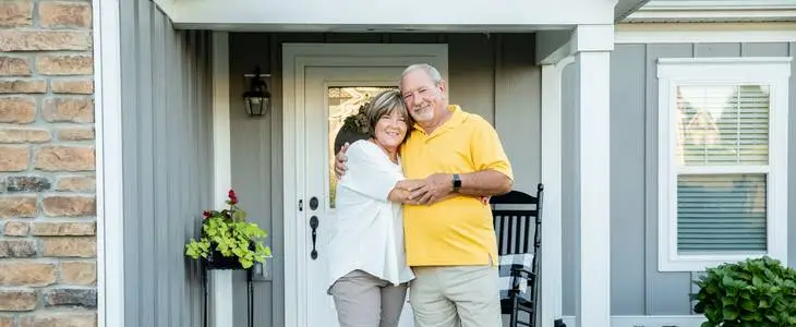 Elderly couple standing in front of their house hugging each other