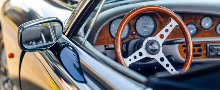 Beautiful wooden steering wheel and and old-fashioned small gauges and large beautiful exterior mirror of a historic cabriolet
