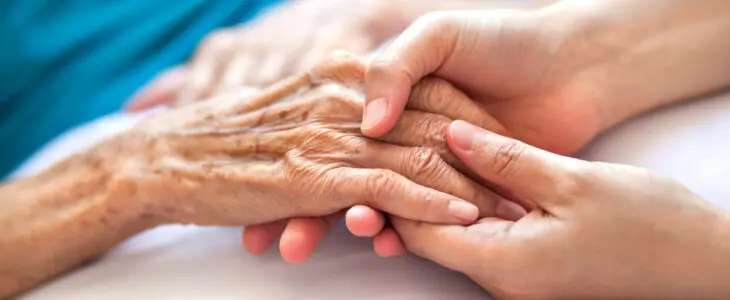 Woman holding senior woman's hand on bed